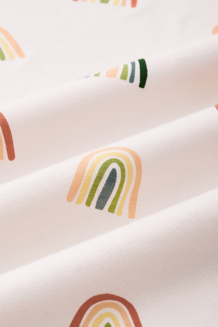 An all-over print featuring alternating rows of boho style rainbows in alternating directions over a light beige background color called Vanilla.Β
One row of rainbows has an outermost arc colored in a dark cool green, followed by a cool sage green, then a light olive green, and finished with an inner core colored in a light apricot.Β
Another row of of rainbows has an outermost arc colored in a burnt orange called Apricot, followed by a light peach, then a light yellow called Lilikoi, and finis
