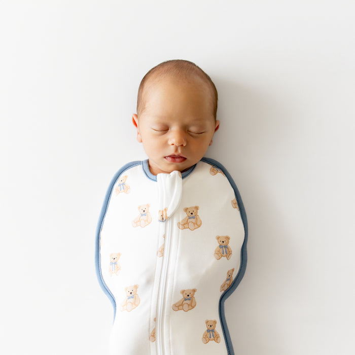 Newborn baby sleeping peacefully in a white swaddle with teddy bear pattern on a light background