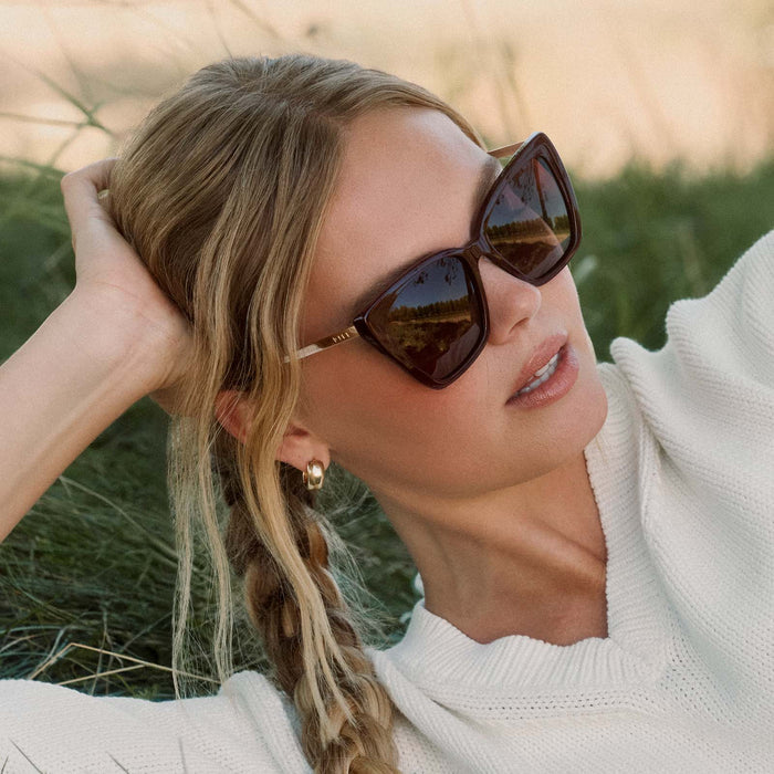 lifestyle - blonde female wearing diff eyewear featuring the becky ii cateye sunglasses with a dark cherry lacquer frame and dark cherry gradient polarized lenses angled view