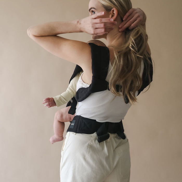 Woman holding a baby in a Boba Auri carrier against a beige background