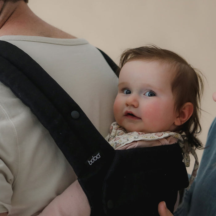 Baby in a Boba Auri black baby carrier with a neutral background
