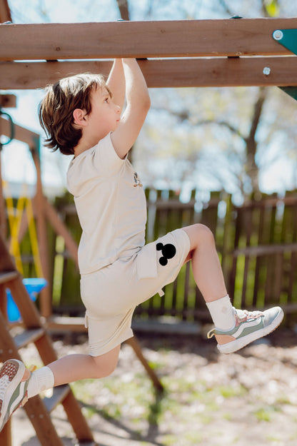 Toddler boy playing on a playground with cream colored cargo shorts with a black mickey head on the short pocket