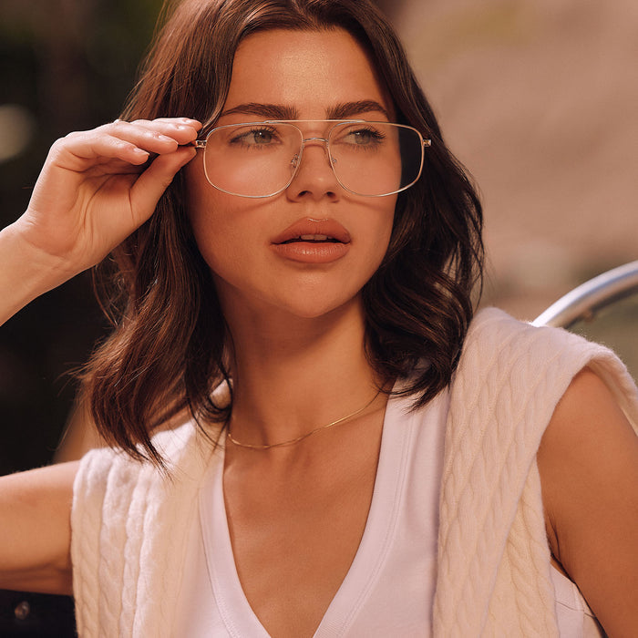 lifestyle - female sitting outside next to her car wearing diff eyewear featuring the charley navigator glasses with a gold metal frame front view