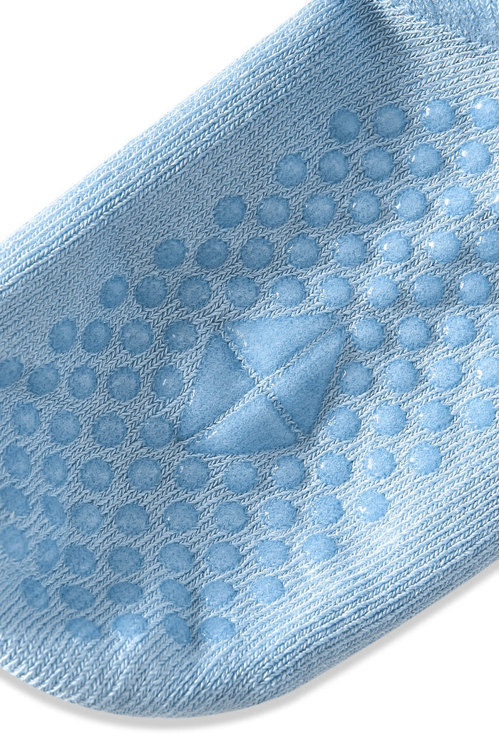 A close-up of a light blue knit sock with a textured grip pattern of raised circular dots and a triangular patch on the sole, shown against a plain white background.
