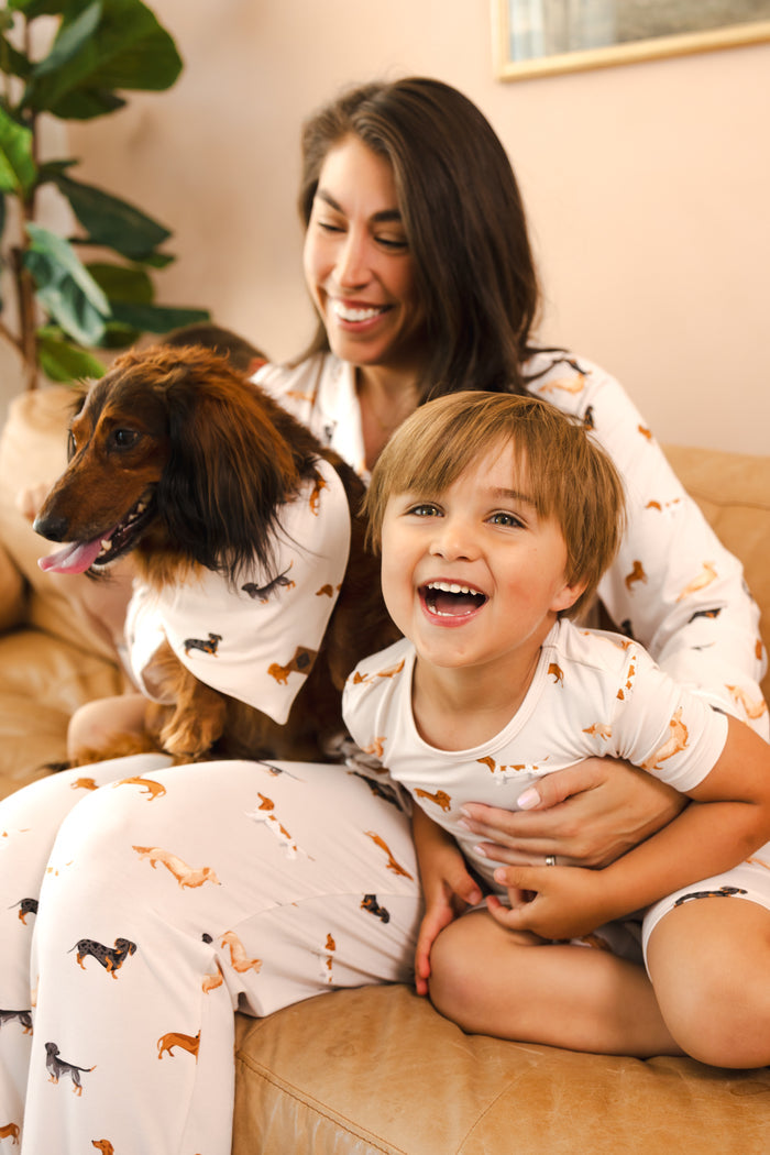 mom and child sitting with their pet dog on a couch wearing wiener dog patterned pajamas
