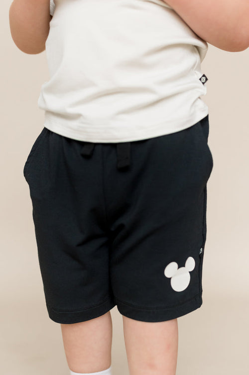 Child wearing black drawstring short with cream colored mickey head on the side of the short