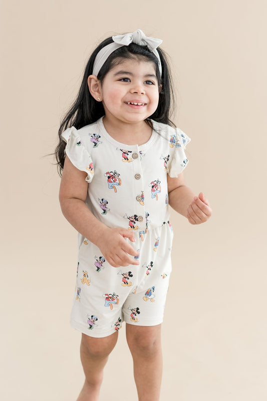 Child wearing mickey mouse and friends printed flutter sleeve romper with buttons on the front and cream bow