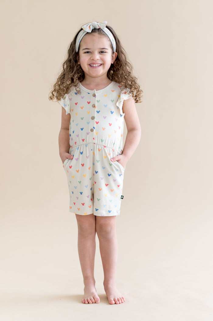 Child wearing cream flutter sleeve romper with a pastel mickey head print