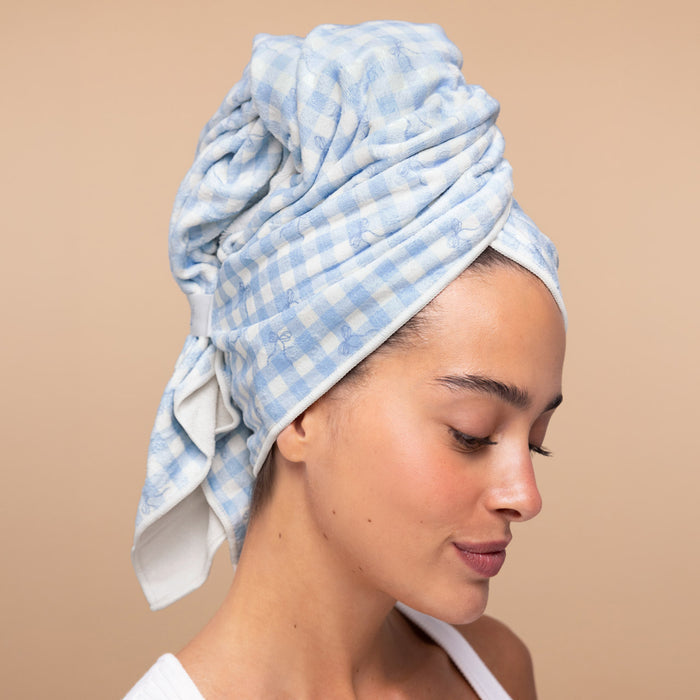 Model with wet hair twisted up in the Kitsch XL Hair Towel Wrap in blue gingham print, secured with the elastic strap after showering
