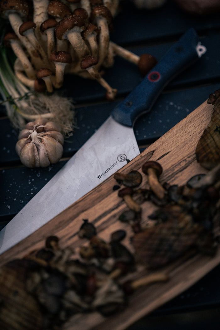 A sharp knife rests on a wooden board with mushrooms and garlic, highlighting a rustic kitchen scene.