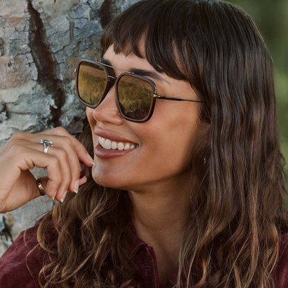 lifestyle - female wearing diff eyewear featuring the jordan navigator sunglasses with a dark cherry lacquer frame and grey gradient polarized lenses angled view outside next to a tree