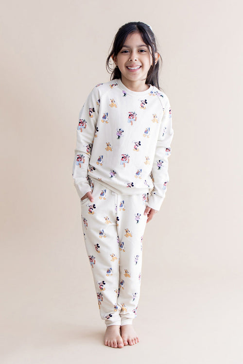 Child wearing a cream jogger set with colorful mickey pattern on a beige background