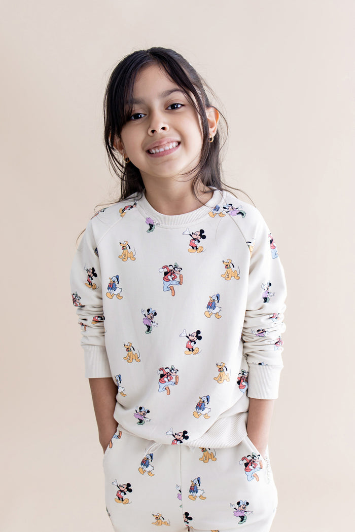 Child wearing a cream sweatshirt with colorful character prints on a beige background