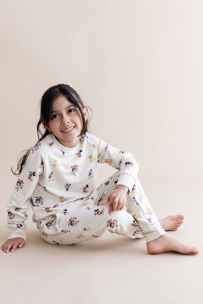 Child wearing a cream mickey character jogger set sitting on a beige surface.