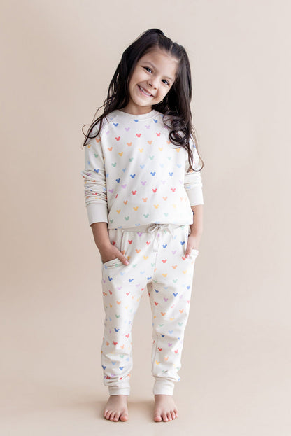 Young girl wearing a cream jogger set with colorful mickey head patterns on a beige background