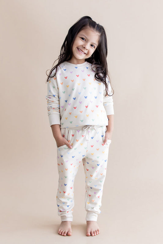 Young girl wearing a cream jogger set with colorful mickey head patterns on a beige background