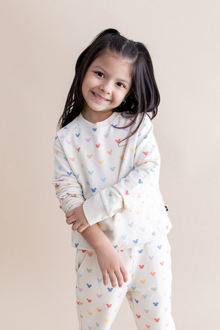 Young girl wearing a cream outfit with colorful mickey patterns on a beige background