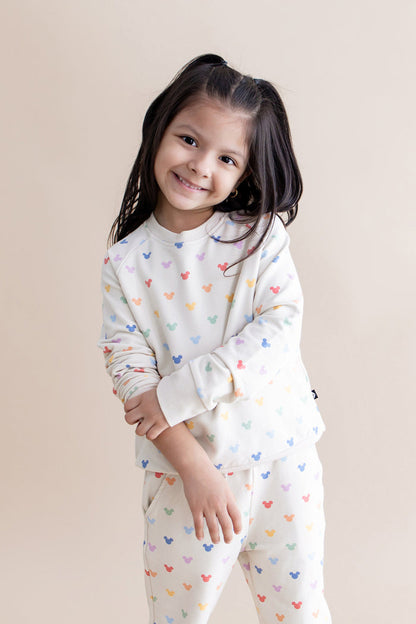 Young girl wearing a cream outfit with colorful mickey patterns on a beige background