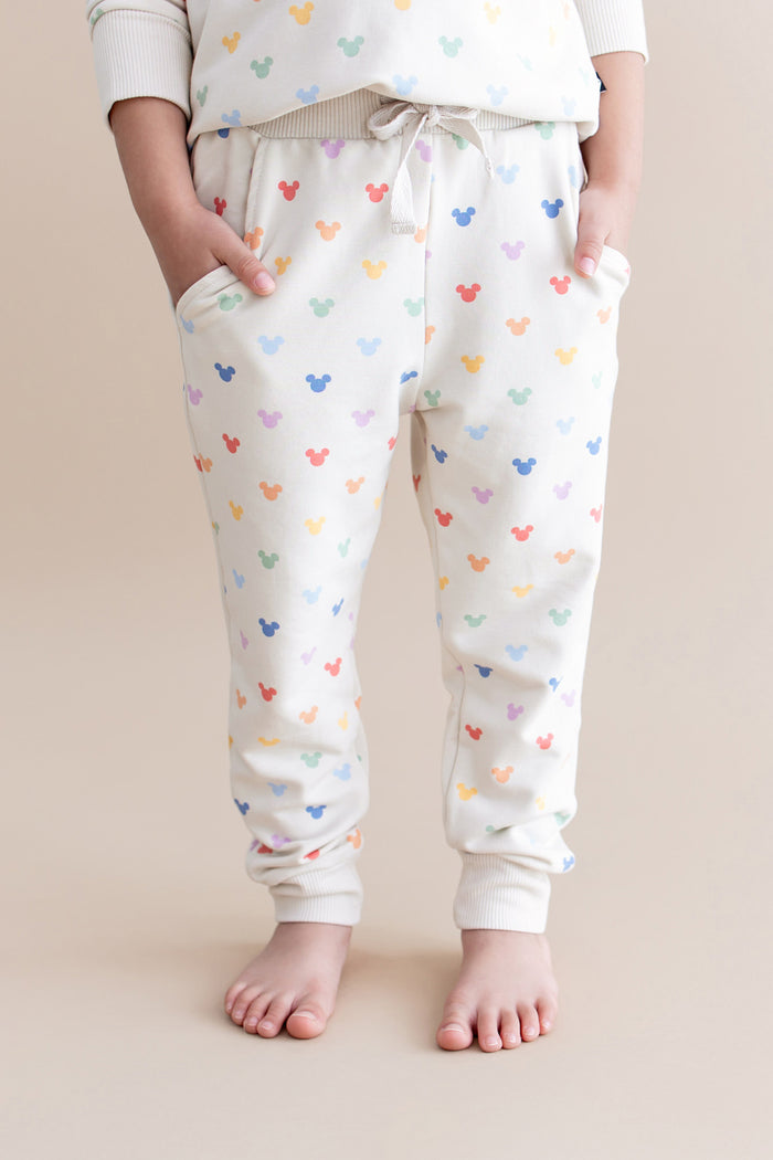 Child wearing jogger pants with colorful mickey pattern on a beige background