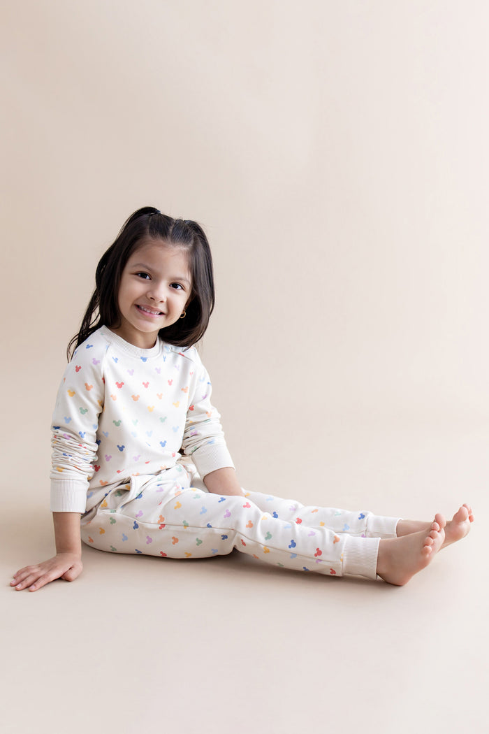 Young girl wearing a cream outfit with colorful mickey head patterns on a beige background