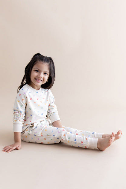 Young girl wearing a cream outfit with colorful mickey head patterns on a beige background