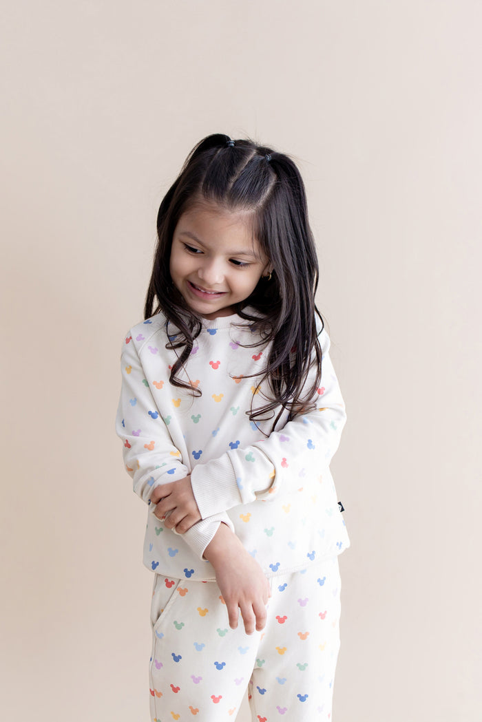 Child wearing a cream outfit with colorful mickey patterns on a beige background