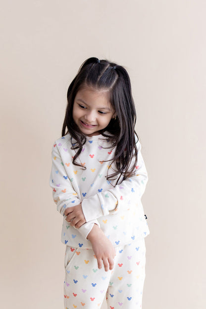 Child wearing a cream outfit with colorful mickey patterns on a beige background