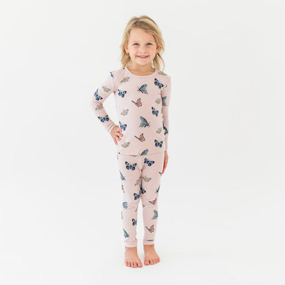 Young girl standing with her hand on her hip wearing the Long Sleeve Pajamas in Blush Butterfly in front of a white background