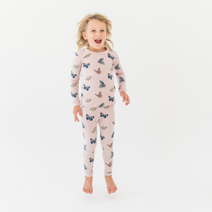 Young girl jumping wearing the Long Sleeve Pajamas in Blush Butterfly in front of a white background