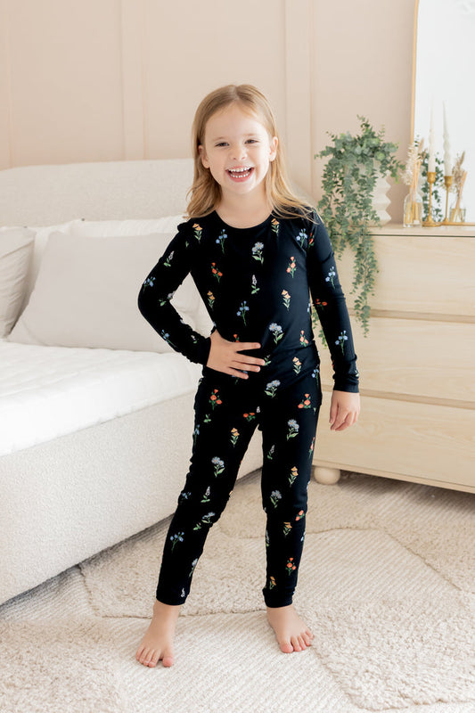 Girl posing in Long Sleeve Pajamas in Midnight Wildflower print standing in a room with white bed