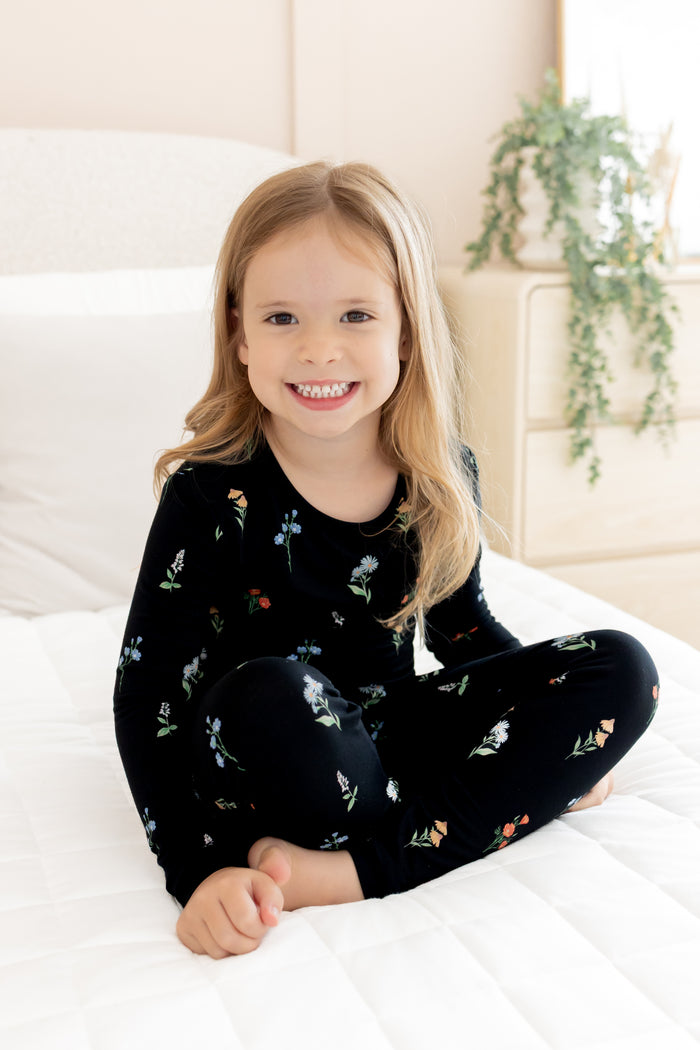 Girl sitting on white bed wearing Long Sleeve Pajamas in Midnight Wildflower print
