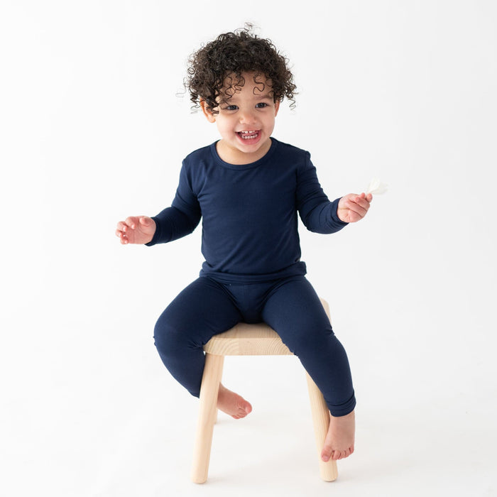 Toddler sitting on a wooden stool while wearing a Long Sleeve Pajama Set in Navy