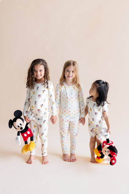 3 Girls standing holding each others hands wearing Long Sleeve Pajamas in in Mickey Mouse & Friends and Pastel Mickey Mouse print and Short Sleeve Pajamas in Mickey Mouse & Friends print holding stuff toys on a white background