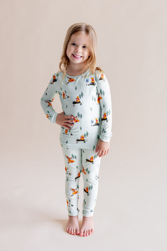Girl posing wearing Long Sleeve Pajamas in Winnie the Pooh Hundred Acre Wood print on a cream background