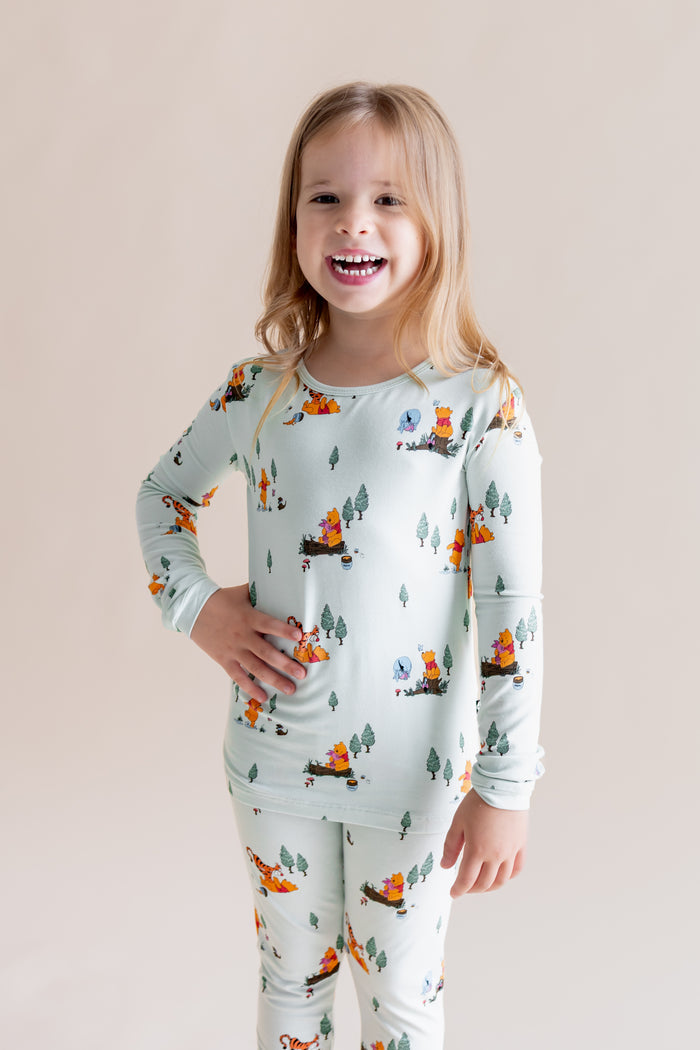 Girl posing in Long Sleeve Pajamas in Winnie the Pooh Hundred Acre Wood print on a cream background