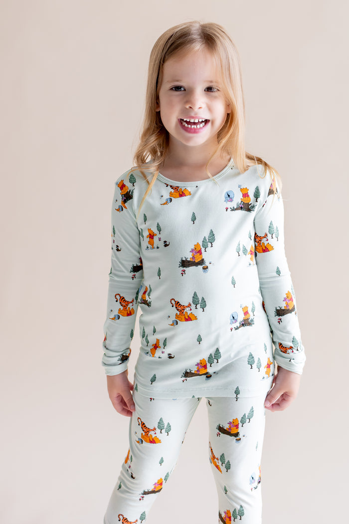 Girl smiling in Long Sleeve Pajamas in Winnie the Pooh Hundred Acre Wood print on a cream background