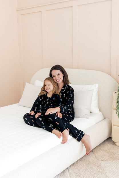 Model and girl wearing matching long sleeve pajama sets in midnight wildflower print cuddling on white bed