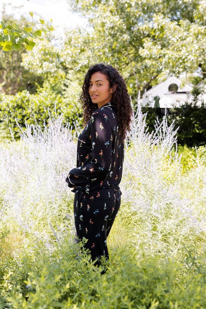 Model posing outdoors in bushes wearing in Long-Sleeved Women's Pajama Set in Midnight Wildflower print