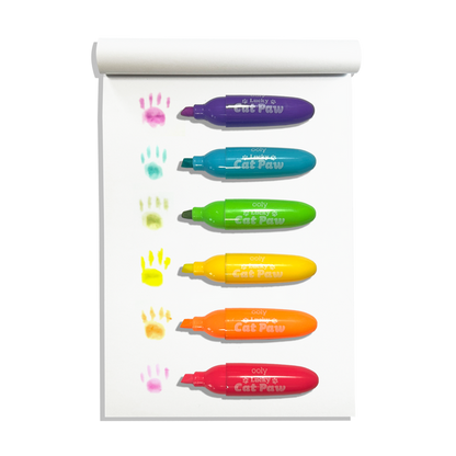 Row of uncapped OOLY Lucky Cat Paw Scented Neon Highlighters on a white sketchbook with cat paw swatches