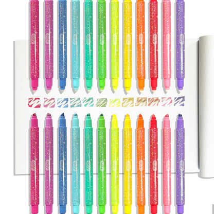 Row of OOLY Make No Mistake! Glittery Erasable Markers uncapped on a white sketchbook showing erasable glitter swatches