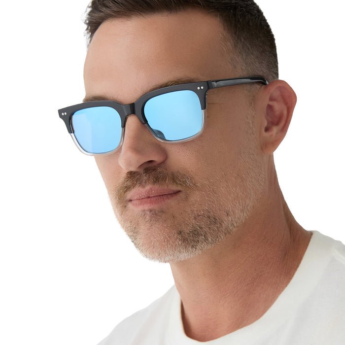 on model - male wearing diff eyewear x fantastic four featuring the mr. fantastic square sunglasses with a black to clear frame and quantum blue mirror polarized lenses angled view