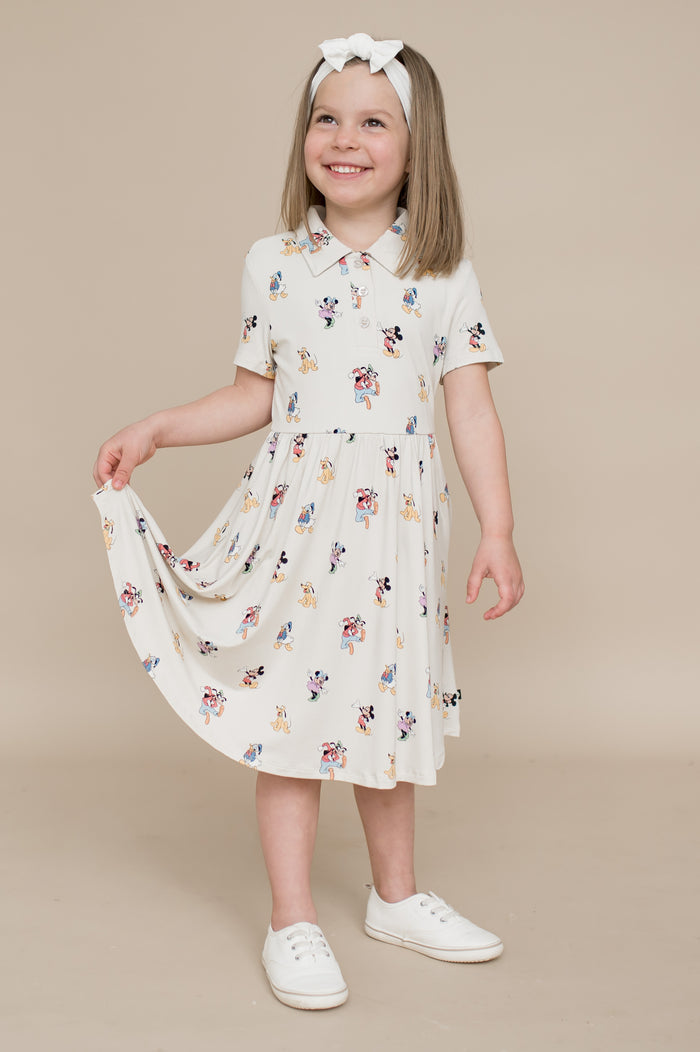 Young girl wearing a cream dress with colorful mickey and friends pattern on a beige background