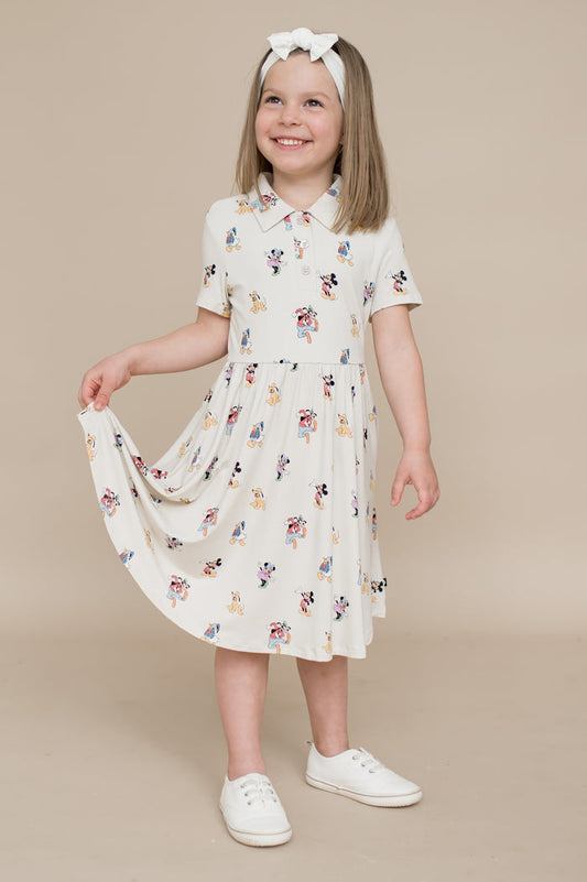 Young girl wearing a cream dress with colorful mickey and friends pattern on a beige background