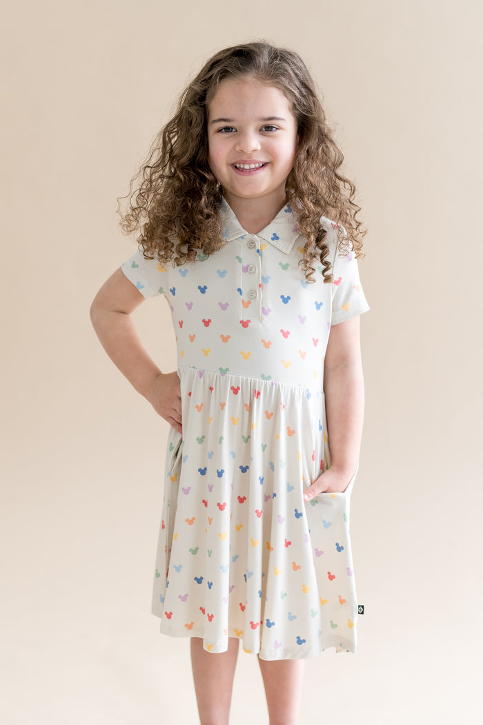 Young girl wearing a cream dress with colorful mickey head patterns against a beige background