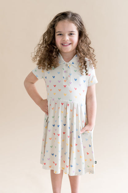 Young girl wearing a cream dress with colorful mickey head patterns against a beige background
