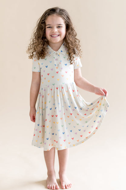 Young girl wearing a cream dress with colorful mickey patterns against a beige background