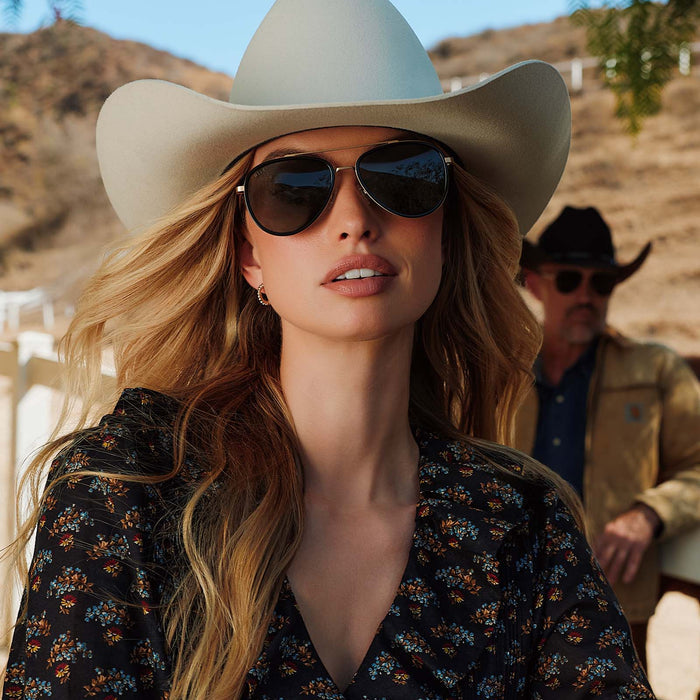 lifestyle - female in a cowboy hat wearing yellowstone x diff eyewear featuring the yellowstone aviator sunglasses with a black frame and g15 polarized lenses front view