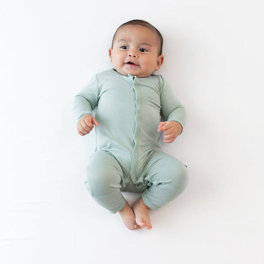 Baby laying on white surface while wearing Kyte Baby  Romper in Sage