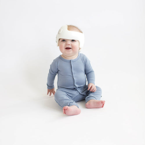Baby sitting in white room wearing a Kyte Baby Romper  in Slate