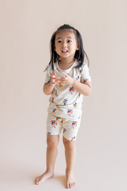Girl wearing Short Sleeve Pajamas in Mickey Mouse & Friends print standing on a cream background